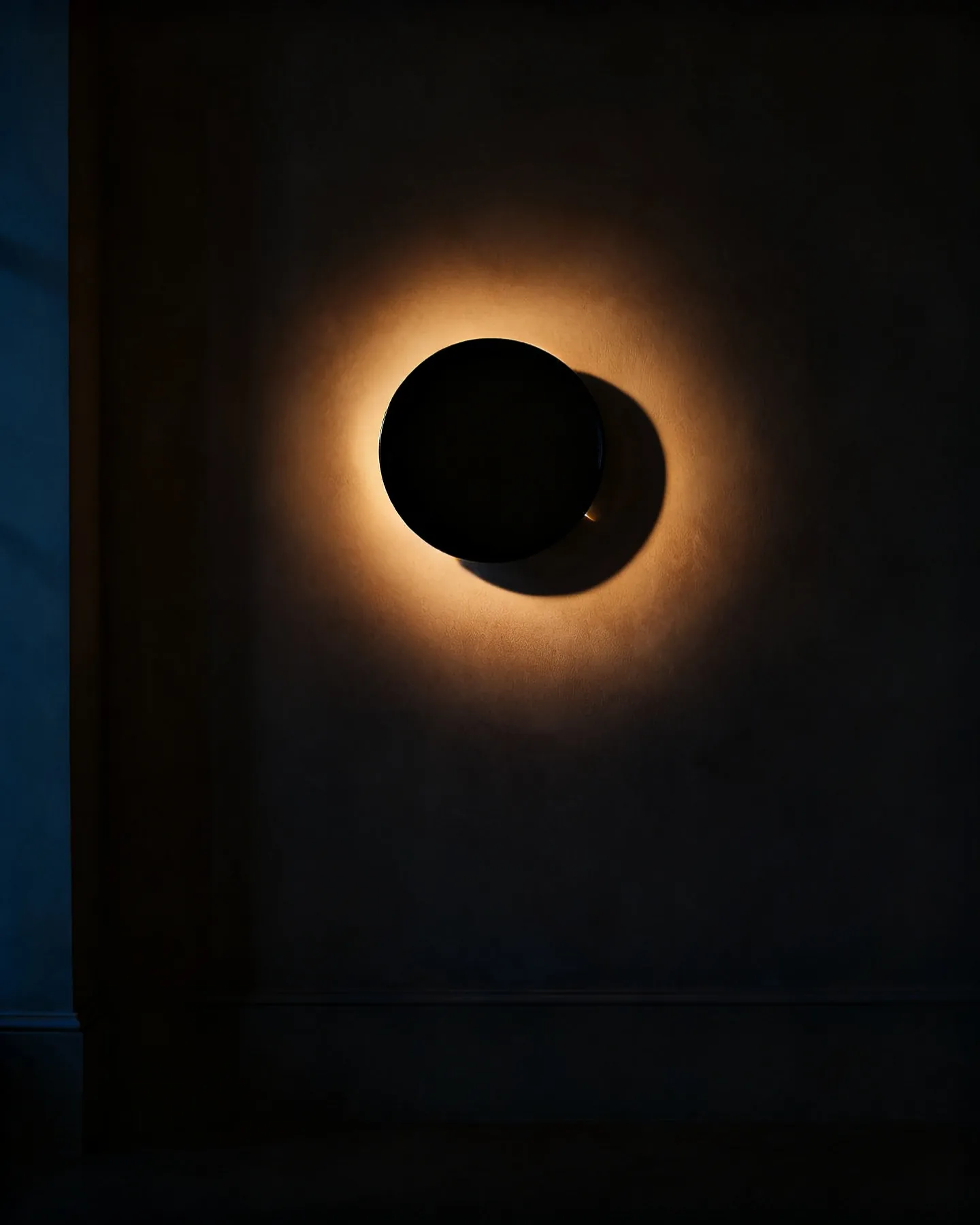 A disc sconce lit from behind, leaving a ring of light on the wall